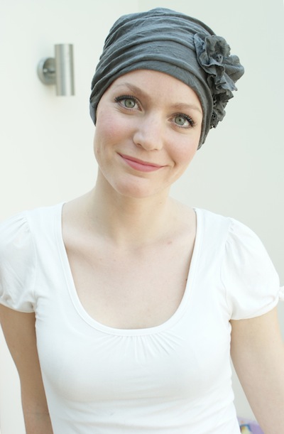 close up of woman smiling wearing brown chemo hat 