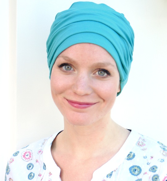 woman smiling wearing teal green chemo beanie