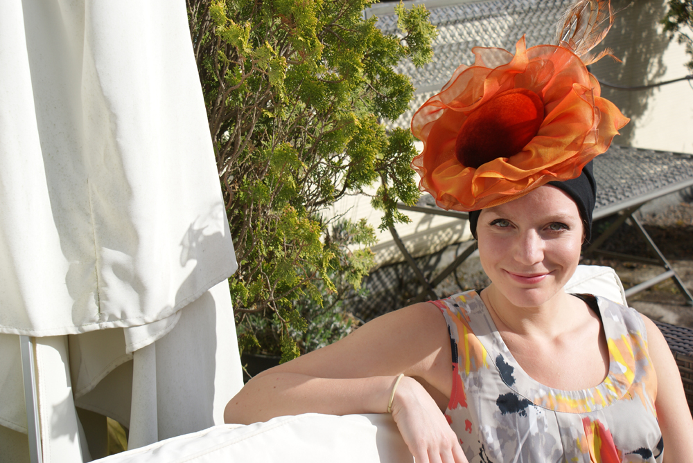 woman sitting in garden wearing orange Ascot hat over turban for hair loss