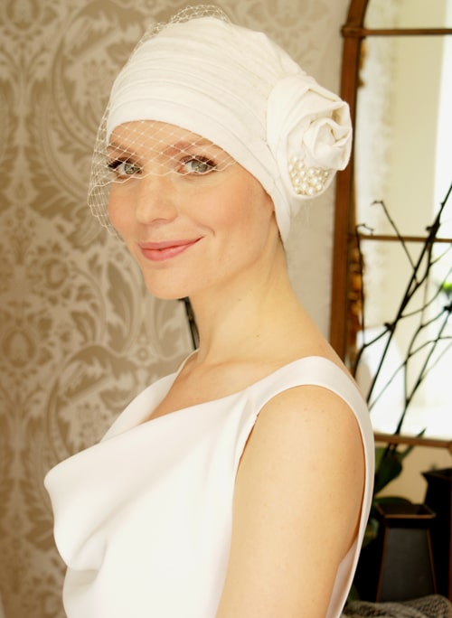 Ivory jersey turban with birdcage veil worn by smiling bride in wedding dress