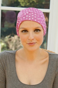 woman seated wearing pink sleep hat with chemo hair loss